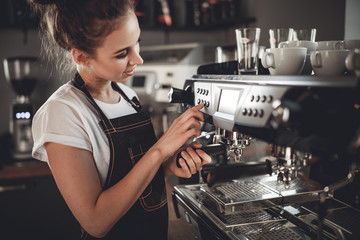 Portrait of professional barista woman in apron making coffee using machine at cafe