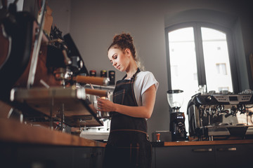 Fototapeta na wymiar Portrait of professional barista woman in apron making coffee using machine at cafe