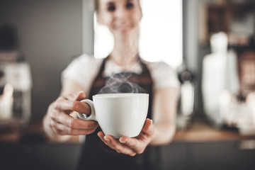 Portrait of professional barista woman in apron holding cup of hot coffee at cafe