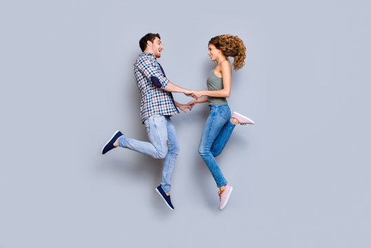 Profile portrait of playful joyful couple in denim outfits sneakers holding hands jumping in air enjoying holiday together isolated on grey background