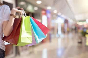 Young woman with shopping bags over shopping mall background - happiness, consumerism, sale season concept