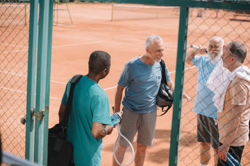 multiracial group of elderly friends with tennis equipment on court