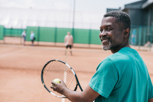 Selective Focus Of Smiling Elderly African American Man Playing Tennis With Friend On Court