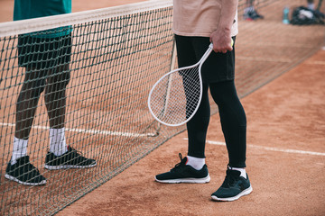 Fototapeta na wymiar cropped shot of interracial friends with tennis racquet standing near net