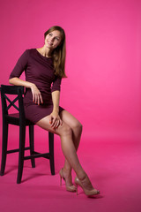 Fototapeta premium beautiful young girl with a smile on her face with flowing hair on a pink background sitting on a chair