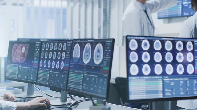  Team of Professional Scientists Work in the Brain Research Laboratory. Neurologists / Neuroscientists Surrounded by Monitors Showing CT, MRI Scans Having Discussions. Shot on RED EPIC-W 8K.