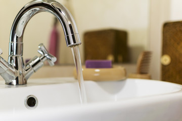 Open modern сhrome faucet with soap in bathroom interior.