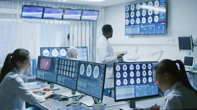 Team of Professional Scientists Work in the Brain Research Laboratory. Neurologists / Neuroscientists Surrounded by Monitors Showing CT, MRI Scans Having Discussions. Shot on RED EPIC-W 8K 