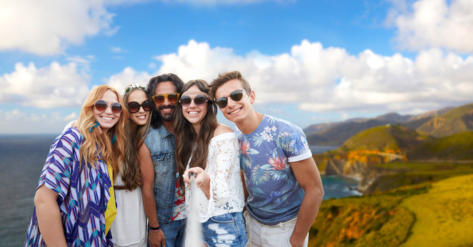 tourism, travel and summer holidays concept - smiling young hippie friends taking picture by selfie stick over big sur coast of california background