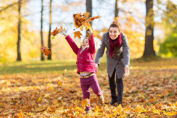 family, season and people concept - happy mother and little daughter playing with autumn leaves at...