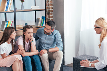 female counselor writing in clipboard while parents cheering up daughter on therapy session