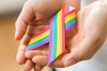 homosexual and lgbt concept - close up of female hands holding gay pride awareness ribbon