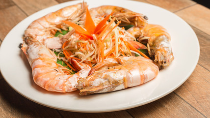 Steamed seafood or Steamed shrimp with herbs and vegetable in white dish on wood table.