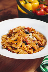Penne pasta in tomato sauce with chicken, tomatoes decorated with parsley on a wooden table