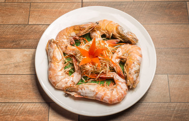 Steamed seafood or Steamed shrimp with herbs and vegetable in white dish on wood table.