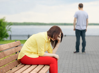 The upset young girl is sitting on a bench in a park. It is concept of the problem relations between a man and a woman.