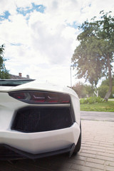 a white sports powerful car looks from behind at the house on the road in sunny weather