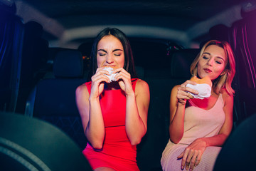 Hungry girl are eating their burgers. They are very concentrated on this process. Brunette girl is...