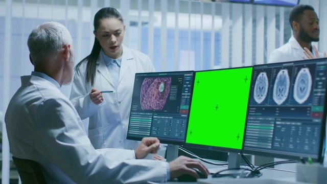 Two Medical Scientists in the Brain Research Laboratory Using Personal Computer with  Green Mock-up Screen. Other Computers Show MRI, CT Scans and Images. Shot on RED EPIC-W 8K Helium Cinema Camera.