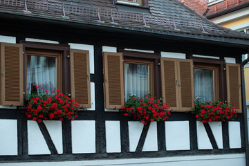 Typisches fränkisches Haus mit roten Blumen an den Fenstern. Die Wand ist weiß mit schwarzen Streifen.