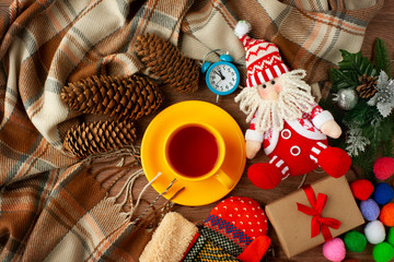 Meet the new year in a cozy atmosphere. A warm plaid, a cup of tea, watches, mittens, fir cones, gifts and a funny Santa Claus create a coziness in the new year.