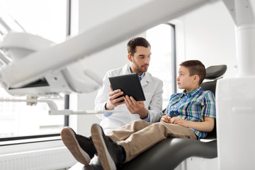 Fototapeta premium medicine, dentistry and healthcare concept - male dentist showing tablet pc computer to kid patient at dental clinic