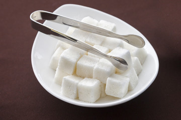 a saucer of sugar cubes and tongs on the table