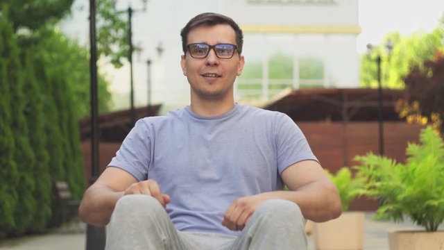 Portrait of an attractive disabled guy with glasses in a wheelchair looking at the camera