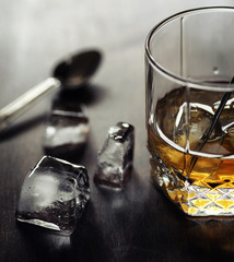 Whiskey with ice with a glass. Cubes of ice on a wooden table an