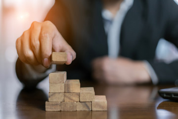Businessman planing and strategy putting wooden blocks risk or success project hands control stack of danger tower challenge game building construction protect at office.
