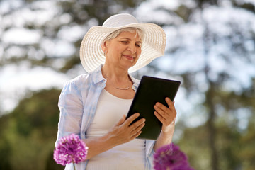 gardening, technology and people concept - happy senior woman with tablet pc computer and flowers at summer garden