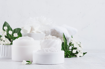 Delicate elegance light cosmetics products for body and skin care with fresh white flowers and green leaves on white wood board, copy space, closeup.