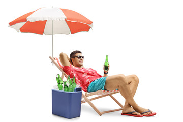 Tourist with a bottle of beer relaxing in a deck chair with an umbrella next to a cooling box