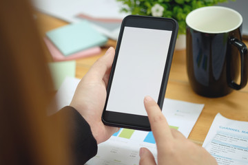 Woman's hand holding white mobile phone  on desk in office