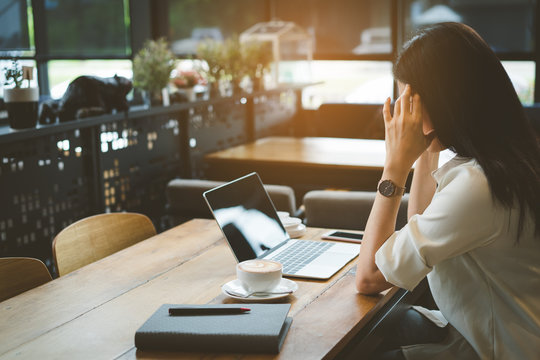 Freelance of businesswoman headache at cafe, Asian female tired,stess or deadline with digital laptop computer and smartphone working on workplace in coffee shop.