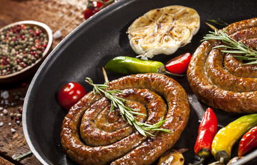 Grilled spiral sausages in a pan on wooden background