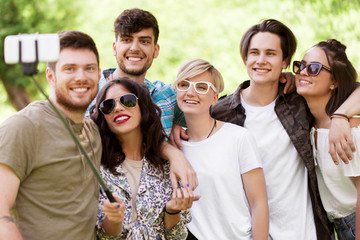 friendship, leisure and technology concept - group of happy smiling friends taking picture by selfie stick at summer park