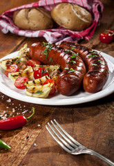 Grilled sausages on a white plate and wooden background