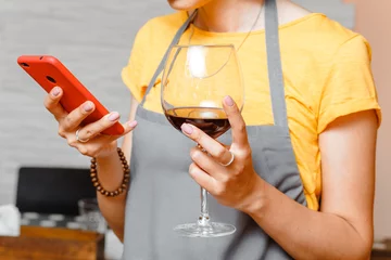 Photo sur Plexiglas Bar woman in apron looking at mobile phone and enjoying glass of red wine