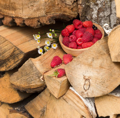 Raspberry berries lie on a bundle of firewood in the garden. Next to the berries lie chamomile flowers