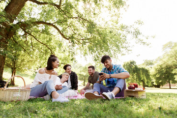 friendship, leisure, technology and people concept - group of friends with smartphones chilling on picnic blanket at summer park - obrazy, fototapety, plakaty
