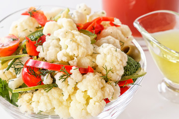 Fresh salad of cauliflower with tomato, broccoli, olives, sweet pepper, greens with a glass of tomato juice and a glass nipple on a white background. Close-up