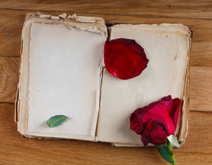 Open old book with blank pages for text and dry rose on wooden table
