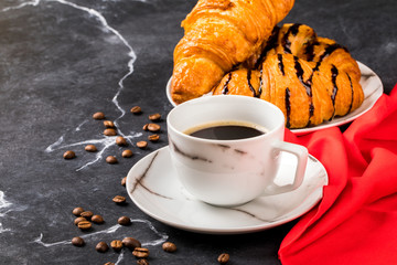 Coffee cup  with chocolate Croissant on a dark marble background with a red napkin. Black espresso.Breakfast. Copy space for Text.