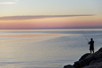 Silhouette of man with fishing spinning. Fishing on the lake at beautiful sunset. Lake Ontario. Rochester, USA