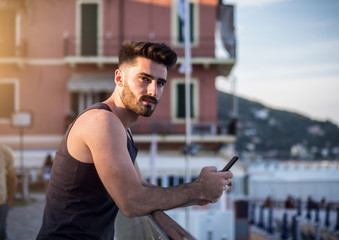 Attractive fit athletic young man at sunset on seaside boardwalk or seafront, wearing black tank-top, looking at camera