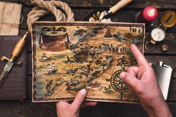 Treasure map in treasure hunter hands. Pirate man learning an old map with red mark.