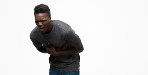 Naklejka premium Young african american man wearing grey t-shirt with hand on stomach because nausea, painful disease feeling unwell. Ache concept.