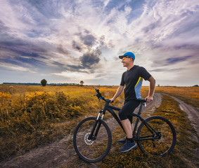 Happy man cyclist rides field road on a mountain bike on the Sunset.