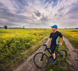Fototapeta na wymiar Happy man cyclist rides field road on a mountain bike on the Sunset.